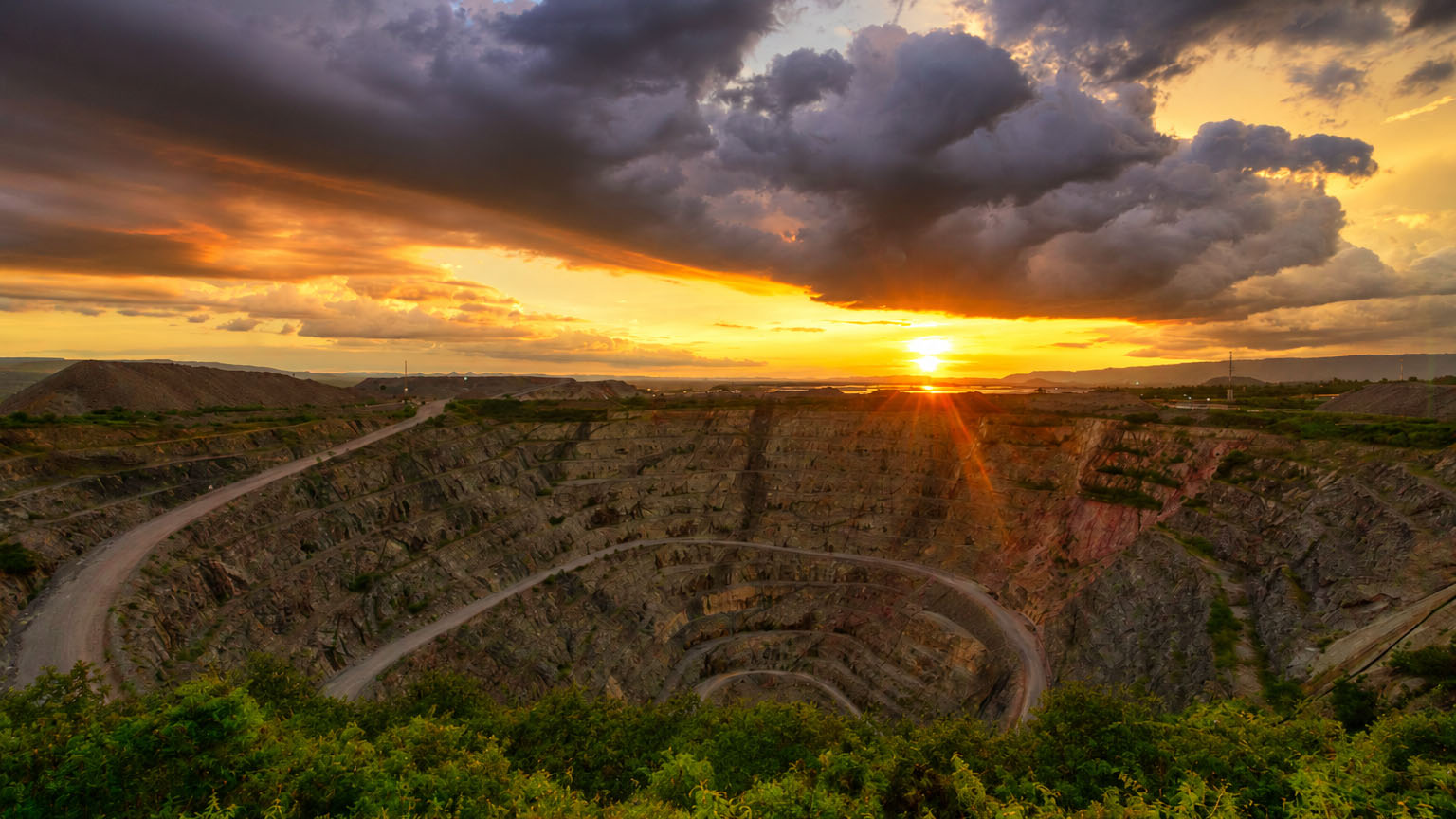 North Mara Gold Mine in Tanzania, with a large open-pit excavation and winding haul roads under a dramatic sunset sky.